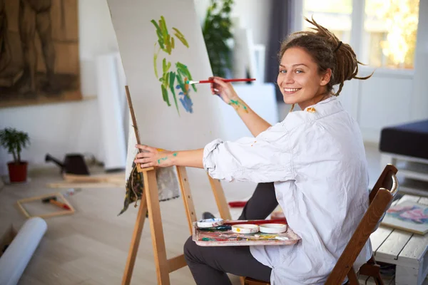 Художественная девушка сидит в студии и рисует на мольберте . — стоковое фото