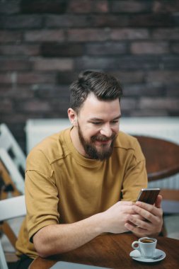 Kafede oturan ve akıllı telefon kullanan genç adam.