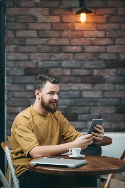 Joven sentado en la cafetería y usando tableta — Foto de Stock