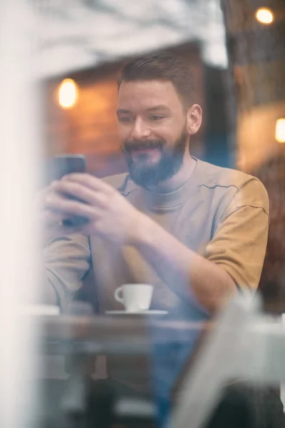 Hombre joven sentado en la cafetería y el uso de teléfono inteligente . — Foto de Stock