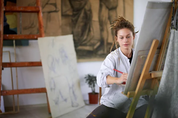 Artystyczny dziewczyna siedzi w studio i malowanie na sztalugach. — Zdjęcie stockowe