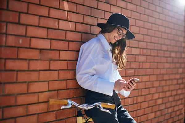 Frau benutzt Smartphone und lehnt sich ans Fahrrad. — Stockfoto