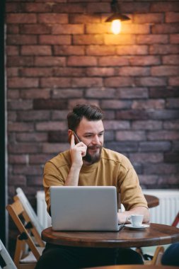 Kafede oturan ve akıllı telefon kullanan genç adam.