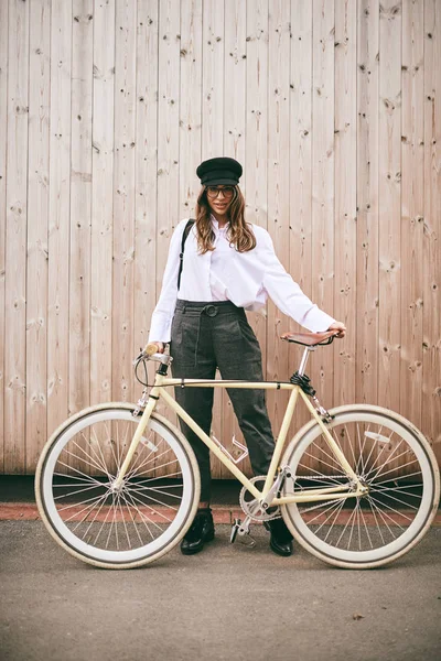 Retrato de bela morena segurando bicicleta. Fundo de madeira — Fotografia de Stock