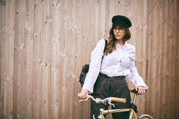 Portrait of beautiful brunette holding bicycle. Wooden backgroun