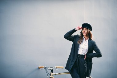 Kadın onun arkasında duvar sarı bisiklet önünde poz... El holding şapkası.