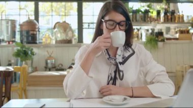 Kafeteryada oturan, kahve içen ve hayali bir dizüstü bilgisayar kullanan beyaz bir iş kadını..