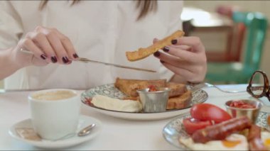 Restoranda otururken beyaz gömlekli bir kadın kahvaltıda Fransız tostu yiyor..