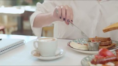 Restoranda otururken beyaz gömlekli bir kadın kahvaltıda Fransız tostu yiyor..