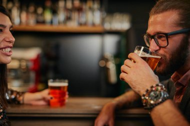 Genç, beyaz sakallı, gözlüklü, bar tezgahına yaslanmış bira içen ve arkadaşlarıyla sohbet eden yakışıklı bir adam..