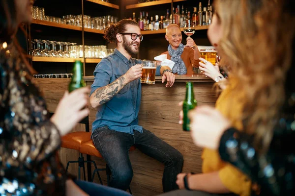 Νεαρός όμορφος καυκάσιος γενειοφόρος άνδρας κάθεται στον πάγκο του μπαρ πίνοντας μπύρα και κουβεντιάζοντας με φίλους. — Φωτογραφία Αρχείου