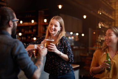 Gülümseyen güzel bir sarışın bar tezgahına yaslanmış, bira şişesi tutuyor ve arkadaşıyla konuşuyor. Gece hayatı..