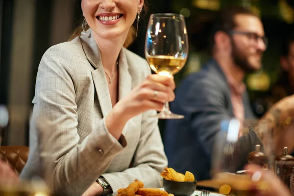 Gehakte foto van mooie Kaukasische brunette gekleed elegant poseren met een glas wijn terwijl zitten in restaurant met haar vrienden. — Stockfoto