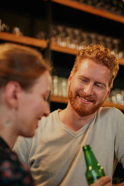 Knappe blanke bebaarde gember die in de bar staat met zijn vriendin, bier drinkt, kletst en plezier heeft. Pub interieur. Uitgaansleven. — Stockfoto