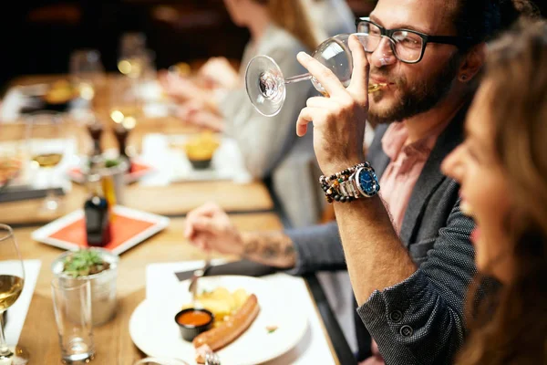 Guapo caucásico barbudo hipster hombre con gafas beber vino mientras se sienta con sus amigos en el restaurante . —  Fotos de Stock