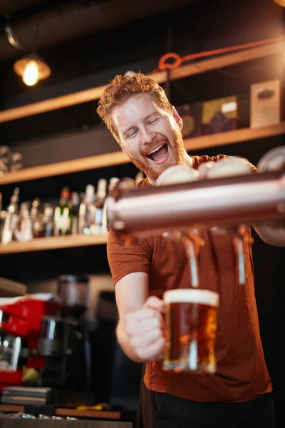 Schöner kaukasischer Barmann, der Bier einschenkt, während er in der Kneipe steht. Selektive Fokussierung auf den Menschen. — Stockfoto