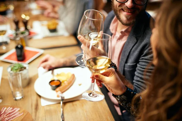 Cropped picture of cute caucasian couple sitting in restaurant and cheering with wine. In background are their friends. — 스톡 사진