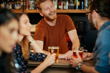 Neşeli arkadaşlar bar tezgahına yaslanır, bira içer ve barmenle sohbet ederler. Gece dışarı.