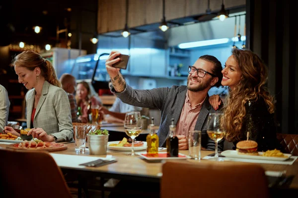 Linda pareja caucásica de moda sentada en el restaurante en la cena y tomando selfie . —  Fotos de Stock