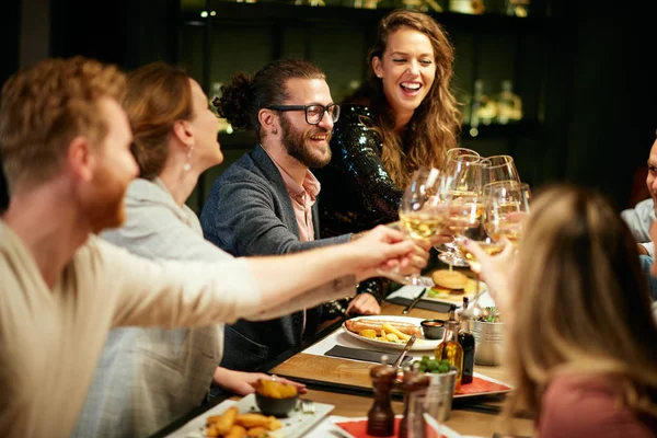 Mejores amigos sentados en el restaurante para cenar y hacer un brindis con vino blanco. En la mesa hay comida. . — Foto de Stock