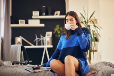 Mavi kazak Charming esmer sabah yatak odasında oturan ve kahve içme.