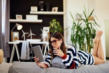 Yatak odasında yatakta mide yatan ve tablet kullanarak kazak Çarpıcı esmer. Sabah saati.