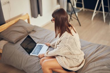 Çekici beyaz esmer yatak odasında yatakta oturan ve dizüstü bilgisayar kullanarak.