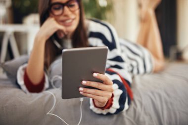 Yatak odasında yatakta mide yatan ve tablet kullanarak kazak Çarpıcı esmer. Sabah saati.