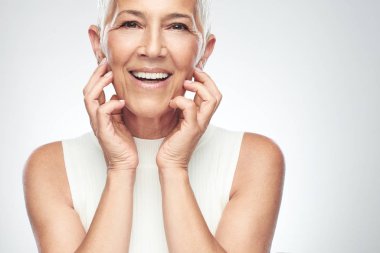 Gri arka plan önünde poz kısa gri saçlı güzel gülümseyen yaşlı kadın. Güzellik fotoğrafçılığı.