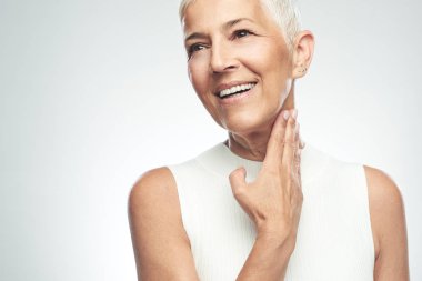 Gri arka plan önünde poz kısa gri saçlı güzel gülümseyen yaşlı kadın. Güzellik fotoğrafçılığı.