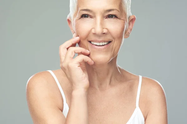 Bella donna anziana sorridente con i capelli corti grigi in posa di fronte a sfondo grigio. Foto di bellezza . — Foto Stock