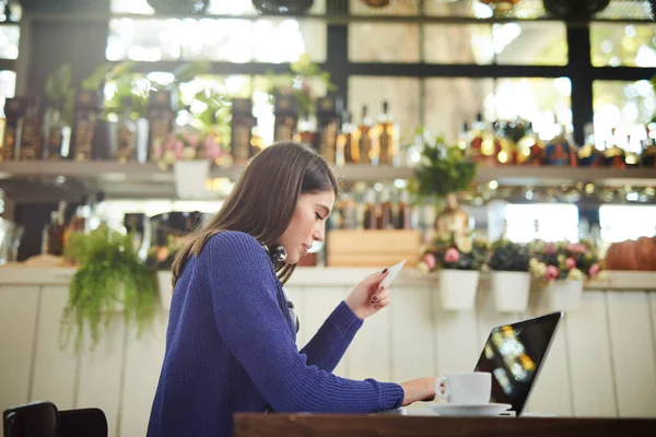 Hermosa morena caucásica elegante en suéter sentado en la cafetería y el uso de ordenador portátil para las compras en línea. En la mano está la tarjeta de crédito . —  Fotos de Stock