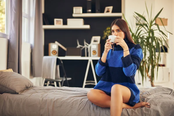 Morena encantadora em camisola azul sentada no quarto de manhã e bebendo café . — Fotografia de Stock