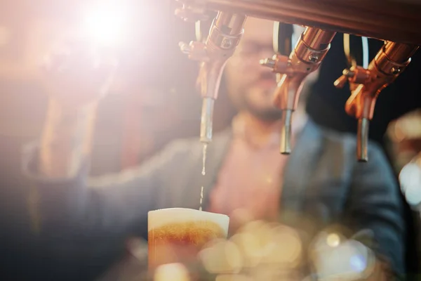 Tatuado barman caucasiano derramando cerveja enquanto estava de pé no pub. Foco seletivo em vidro . — Fotografia de Stock