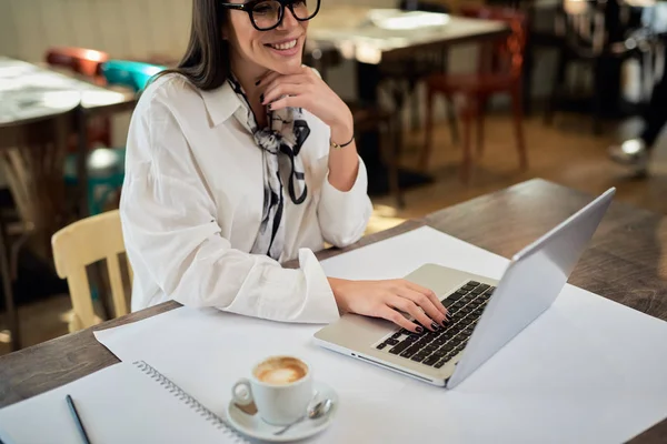Ελκυστική επιχειρηματίας που κάθεται στο καφέ και χρησιμοποιεί φορητό υπολογιστή. Στο τραπέζι είναι laptop, notebook και φλιτζάνι καφέ. Τα χέρια είναι στο πληκτρολόγιο. — Φωτογραφία Αρχείου