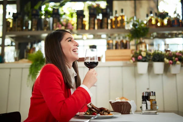 Retrato de bela morena caucasiana de terno sentado no restaurante e segurando copo de vinho tinto . — Fotografia de Stock