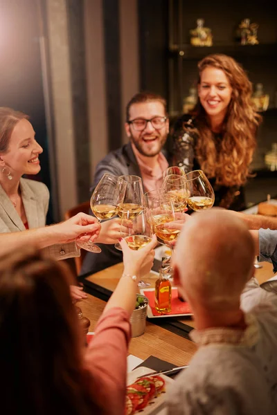 Nejlepší přátelé sedící v restauraci na večeři a pronášející přípitek s bílým vínem. Na stole je jídlo. — Stock fotografie