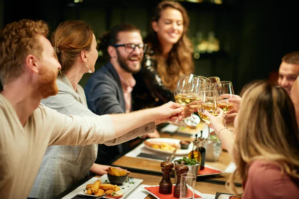 Mejores amigos sentados en el restaurante para cenar y hacer un brindis con vino blanco. En la mesa hay comida. . — Foto de Stock