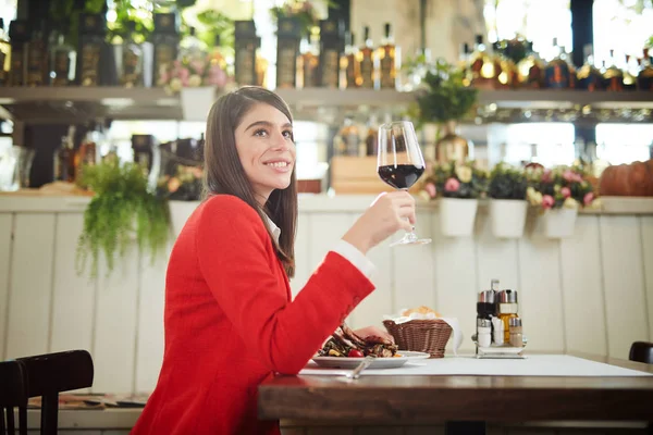 Gelukkig aantrekkelijke Kaukasische zakenvrouw in pak zitten in restaurant voor lunch pauze en het drinken van rode wijn. — Stockfoto