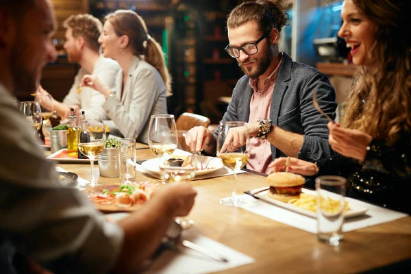 Un grup vesel de prieteni care iau cina la restaurant. Ei mănâncă, vorbesc, zâmbesc și se distrează de minune. . — Fotografie, imagine de stoc