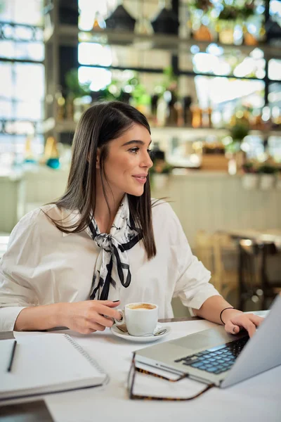 CEO caucasiano atraente sentado no café, segurando xícara de café e usando laptop para o trabalho. Conceito de trabalho duro . — Fotografia de Stock