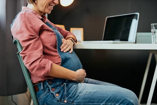 Proud future mother sitting in her home office and touching belly. — Stock Photo, Image