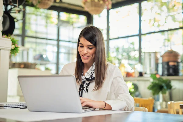 Mulher de negócios atraente sentado no café e usando laptop. Na mesa estão laptop, notebook e xícara de café. As mãos estão no teclado . — Fotografia de Stock