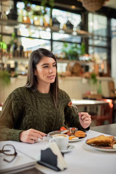 Attractive brunette sitting in restaurant in morning and eating breakfast. — Stock Photo, Image