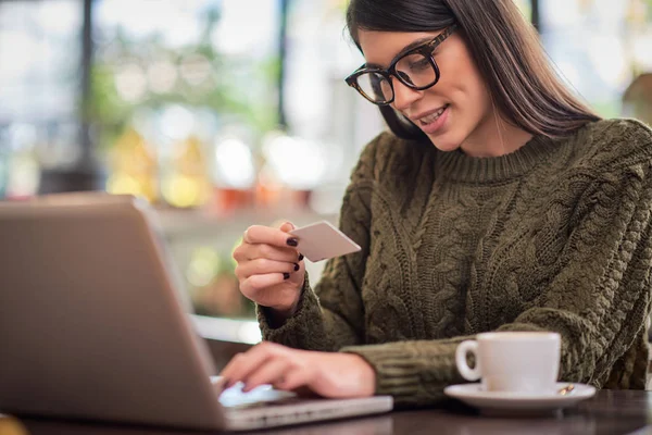 Attraente bruna caucasica in maglione seduta nel caffè, digitando sulla tastiera e tenendo in mano la carta di credito . — Foto Stock