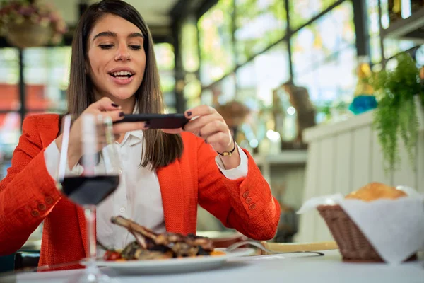 Attraktiv affärskvinna i kostym sitter i restaurang och tar bild av mat via smartphone. — Stockfoto