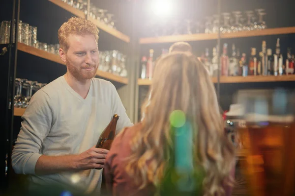 Посміхнена кавказька пара стоїть у барі, фліртує і тримає пивні пляшки.. — стокове фото