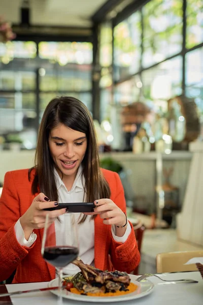 Aantrekkelijke zakenvrouw in pak zitten in restaurant en het nemen van foto van voedsel via de smartphone. — Stockfoto