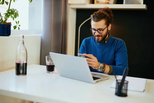 Attraktiv kaukasisk skäggig entreprenör sitter på sitt kontor, använder smart telefon och tar en paus från jobbet. — Stockfoto