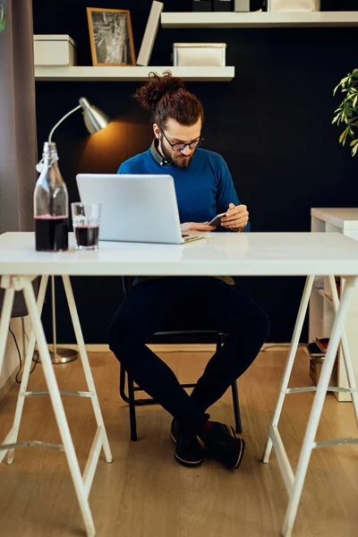 Jonge blanke zakenman zit in zijn moderne kantoor, met behulp van een smartphone en het nemen van een pauze van het werk. — Stockfoto